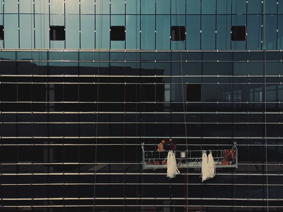 Close-up of hand cleaning window with squeegee outdoors using yellow gloves.